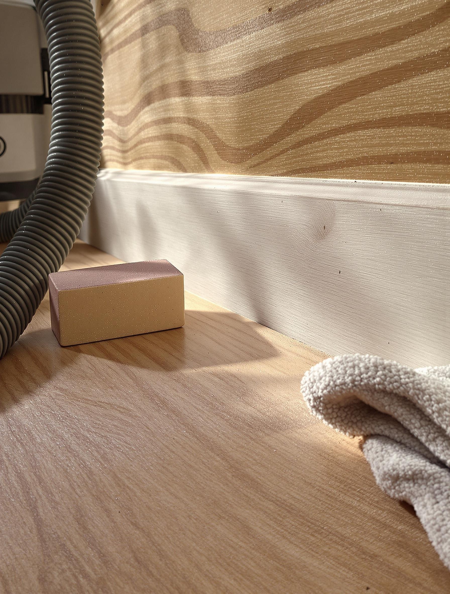 Atelier bricolage : cale-ponce, aspirateur et chiffon microfibre près d’une coupe de plinthe