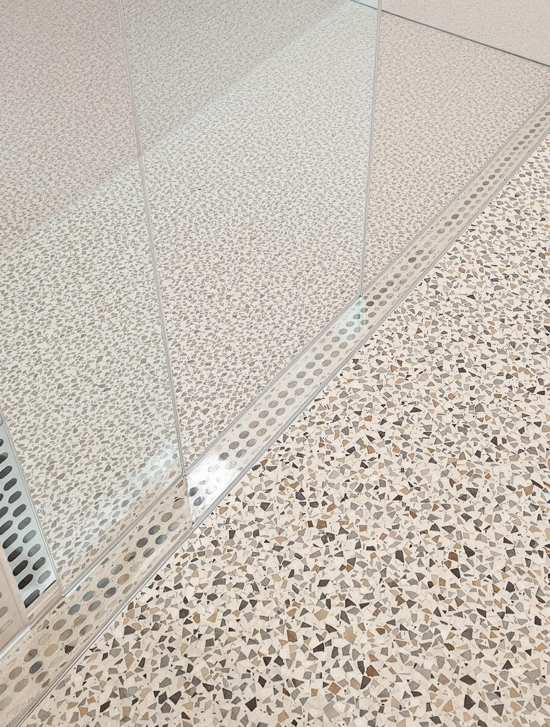Gros plan sur un sol de douche à l'italienne avec carrelage terrazzo antidérapant et caniveau inox moderne.